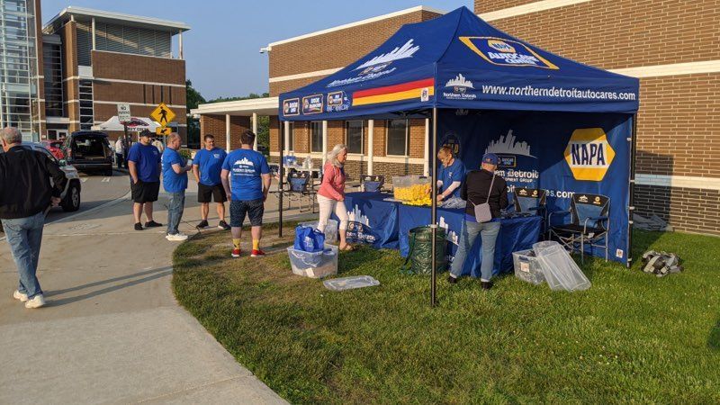 A NAPA auto parts tent set up outside, people gathering around, on a sunny day.