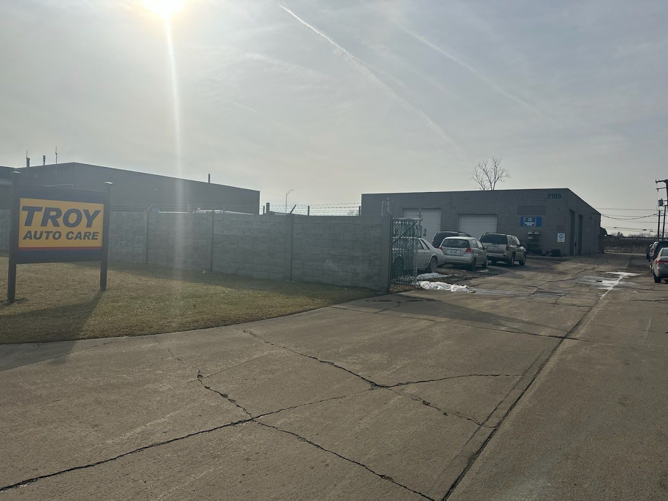 Troy Auto Garage sign in front of a gray building and a paved driveway. Cars are parked nearby.