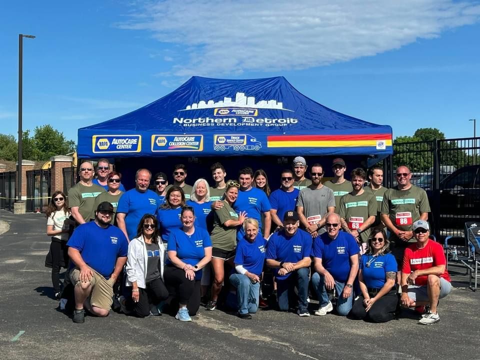Group of people in blue and green shirts pose in front of a blue Northern Energy tent on a sunny day.