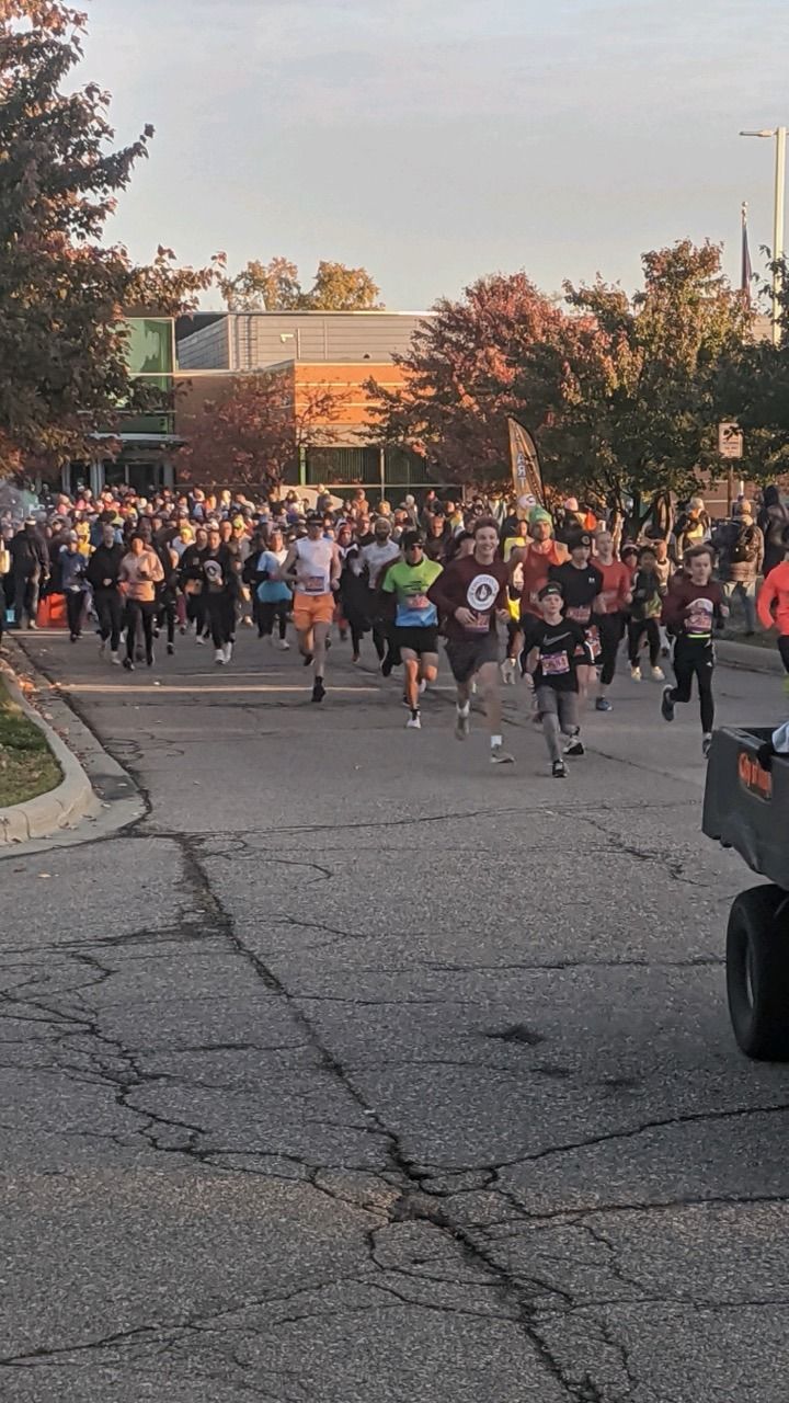Runners at a race, on a cracked road, with buildings and spectators in the background.