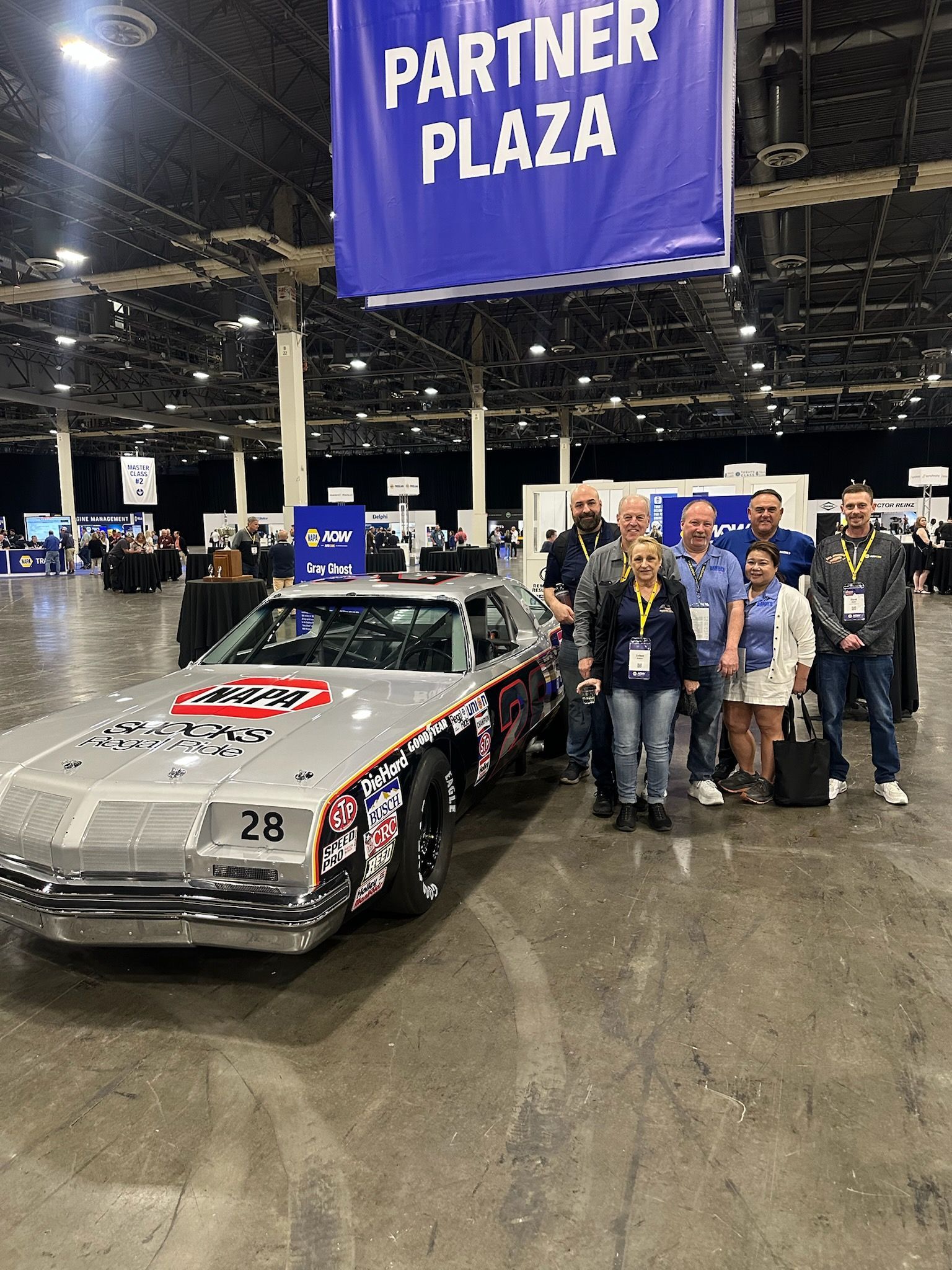 Group of people standing near a race car in a Partner Plaza area.