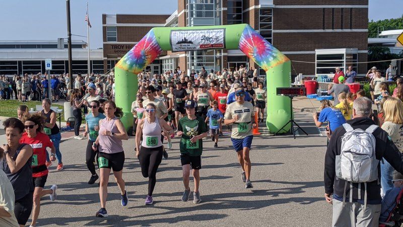Runners in a race under a tie-dye arch. Crowd of people, building in background.