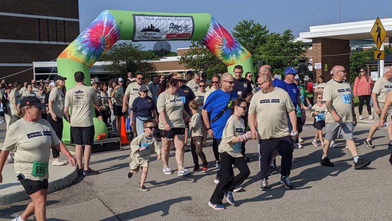 People walking/running under a tie-dye archway at an outdoor event. Many wear matching shirts.