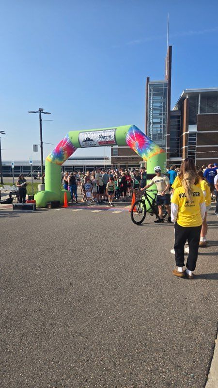 People gathered at the start line of a race under a colorful inflatable arch on a sunny day.