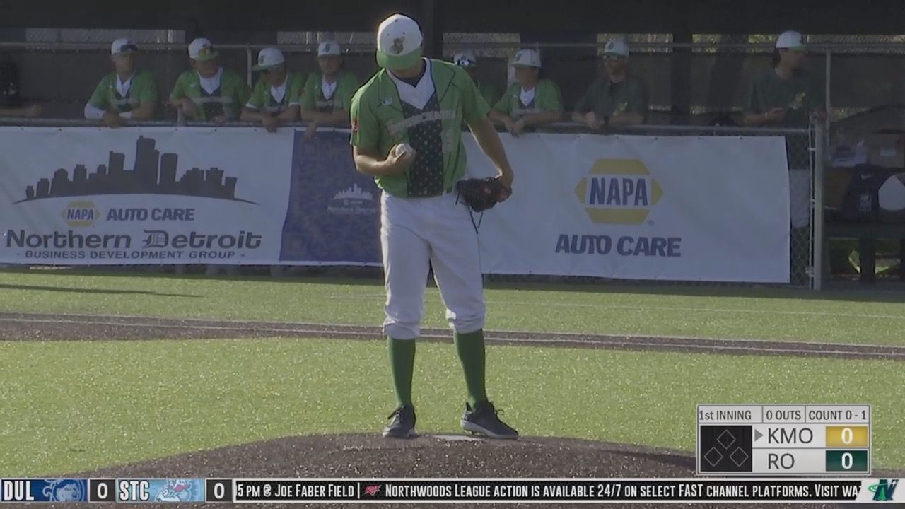 Baseball pitcher in green jersey, white pants, and green socks winding up to throw.