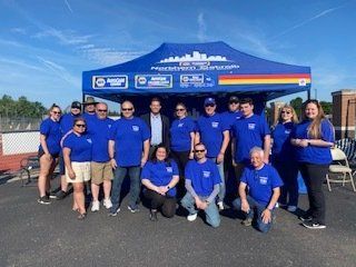 Group of people in blue shirts pose under a tent with cityscape logo.