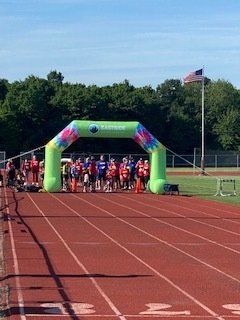 Runners at a track start line under an inflatable archway on a sunny day.