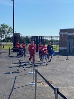 People in red shirts walking through an open gate on a sunny day.