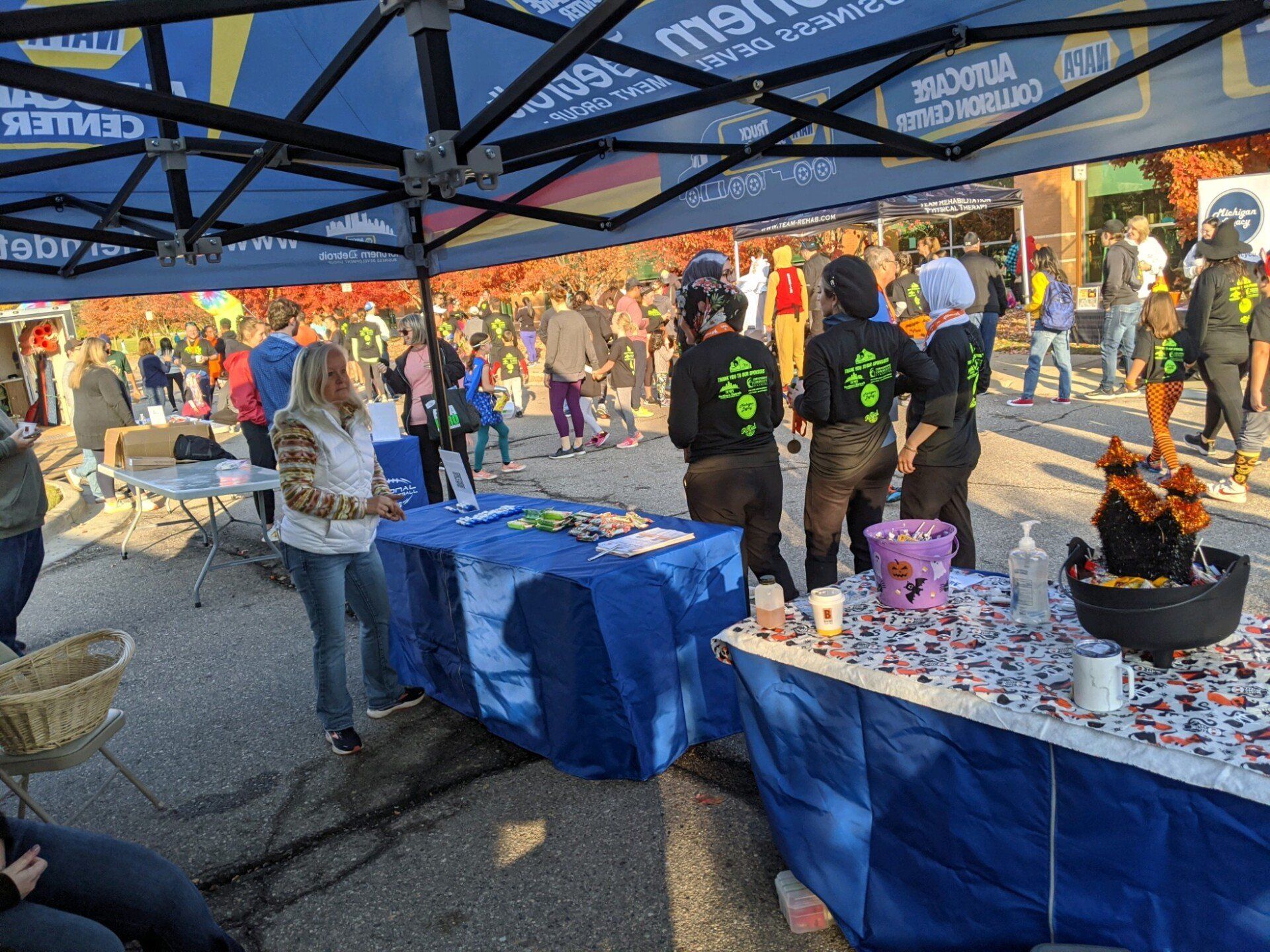 Outdoor event with blue tent, tables, and people in the background; some staff wearing black shirts.
