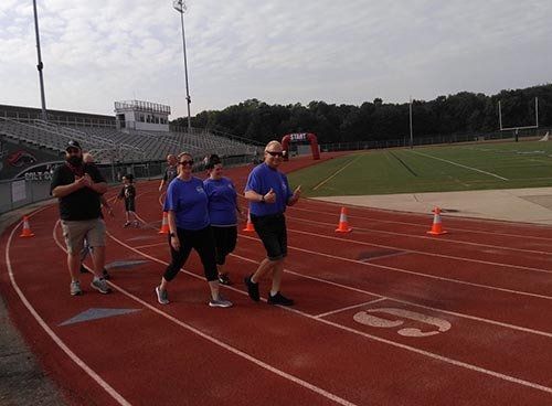 People in blue shirts walking on a red track; stadium in the background.