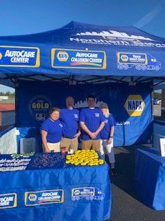 People in blue NAPA shirts at a tent. Blue and yellow logo. Outdoor event, sunny.