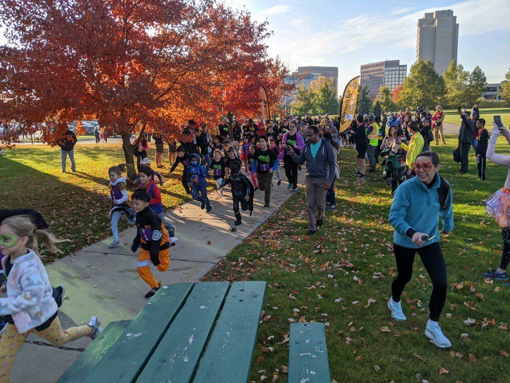 People running in a park; autumn leaves and cityscape in the background.