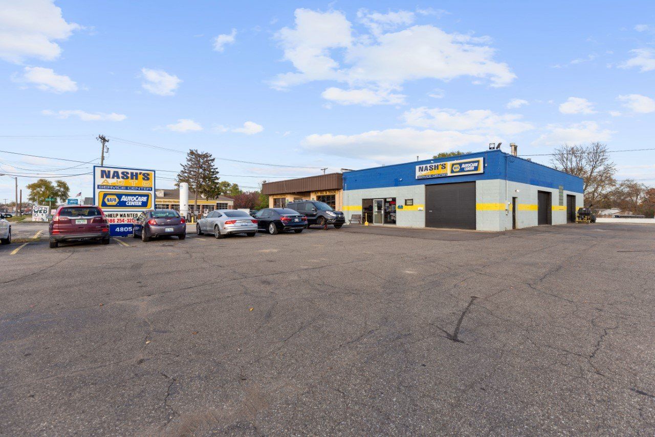 Auto repair shop exterior with sign, cars parked out front, and blue and yellow building against a cloudy sky.