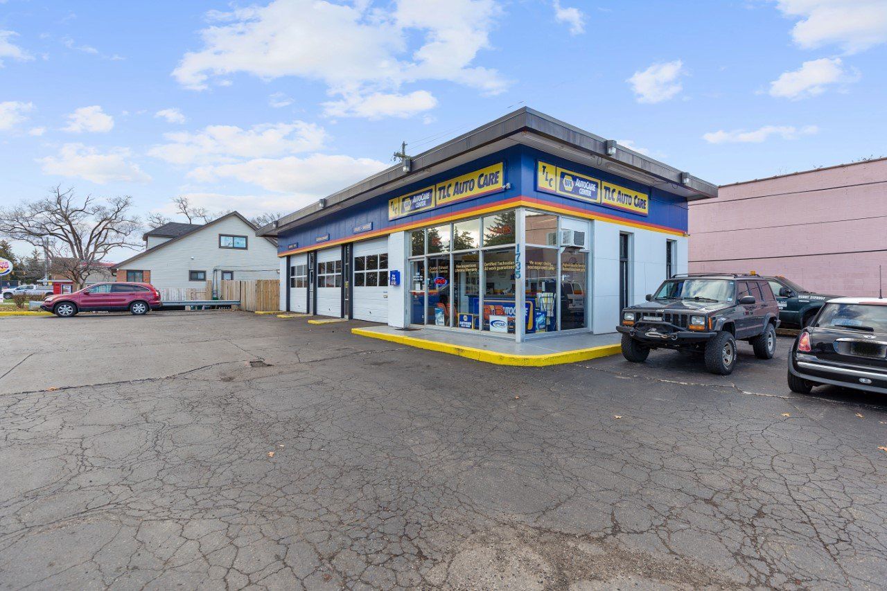 Exterior view of an auto repair shop with parked cars. Building has large windows and a blue and yellow awning.