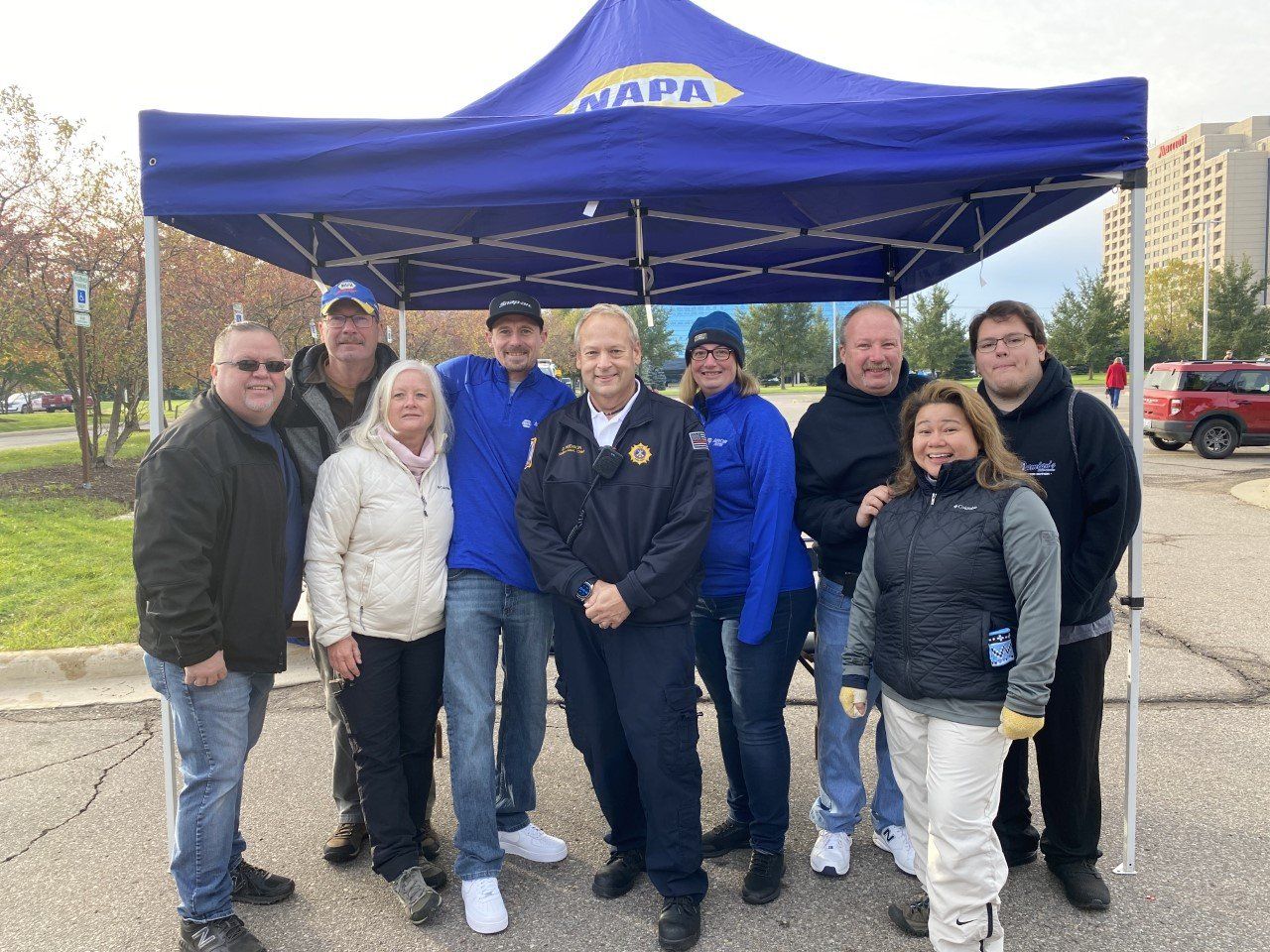 Group of people under a blue NAPA tent, smiling outside a building.