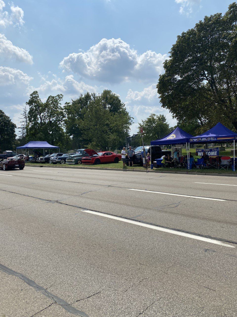 Car show with cars parked near blue tents on a sunny day.