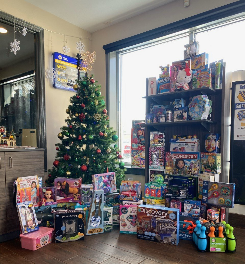 Christmas tree and toys in a room. Many wrapped presents. Shelves full of toys.