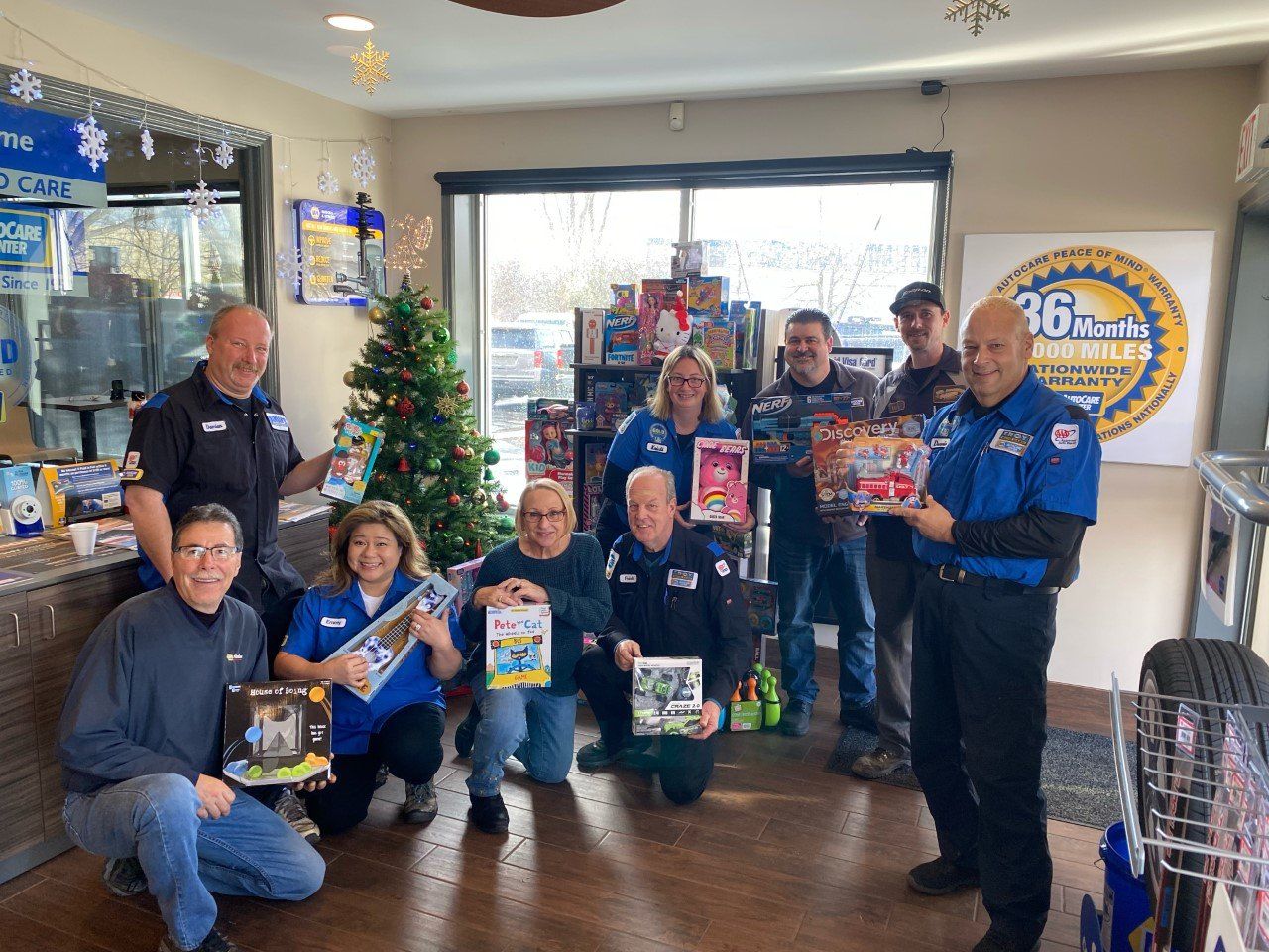 People at a shop holding donated toys near a Christmas tree.