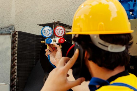 Technician in yellow hard hat inspecting pressure gauges on industrial equipment