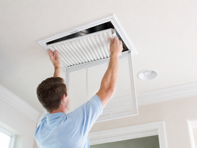 Person replacing a ceiling air filter in a white home ceiling vent