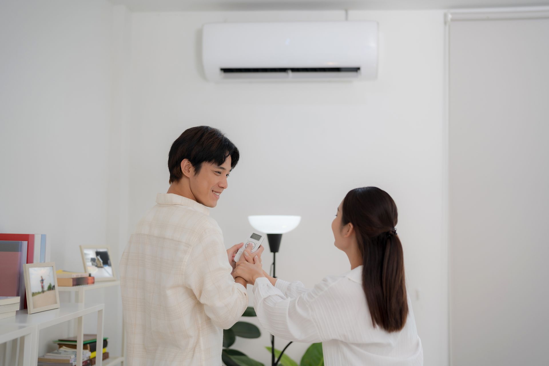 Two people in a bright room looking at a laptop under a wall-mounted air conditioner