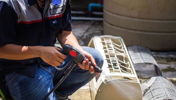 Person using a power drill to work on a beige plastic container outdoors.
