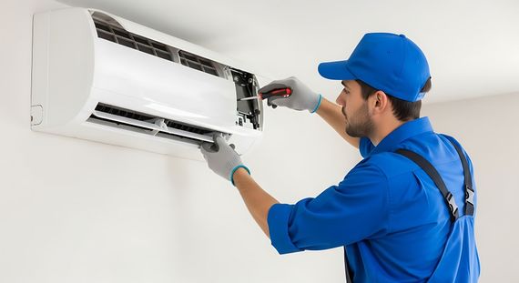 Technician in blue uniform repairing a wall-mounted air conditioner with tools