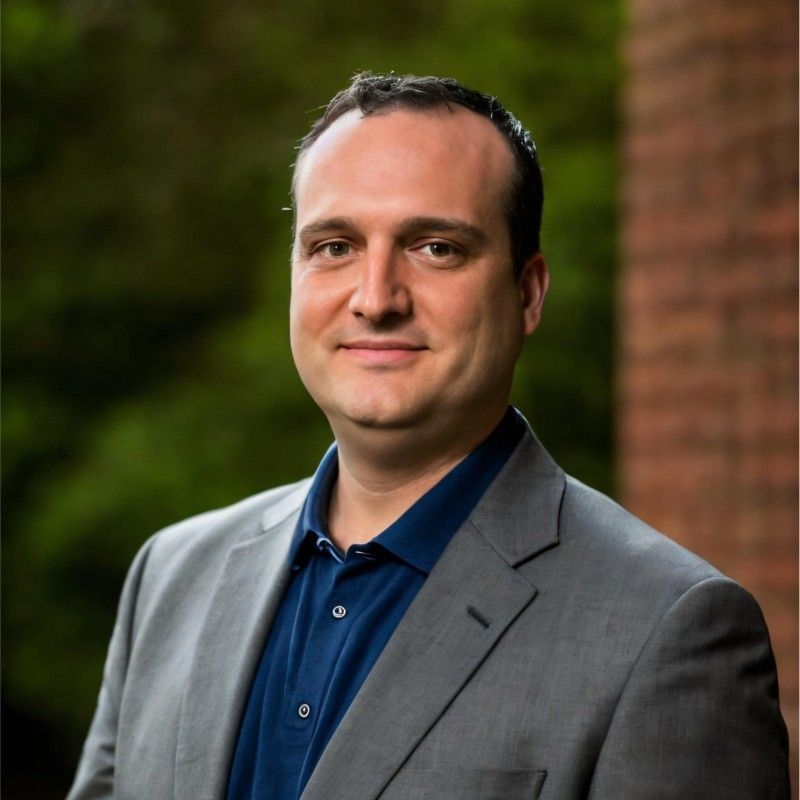 A man in a suit and blue shirt is smiling for the camera