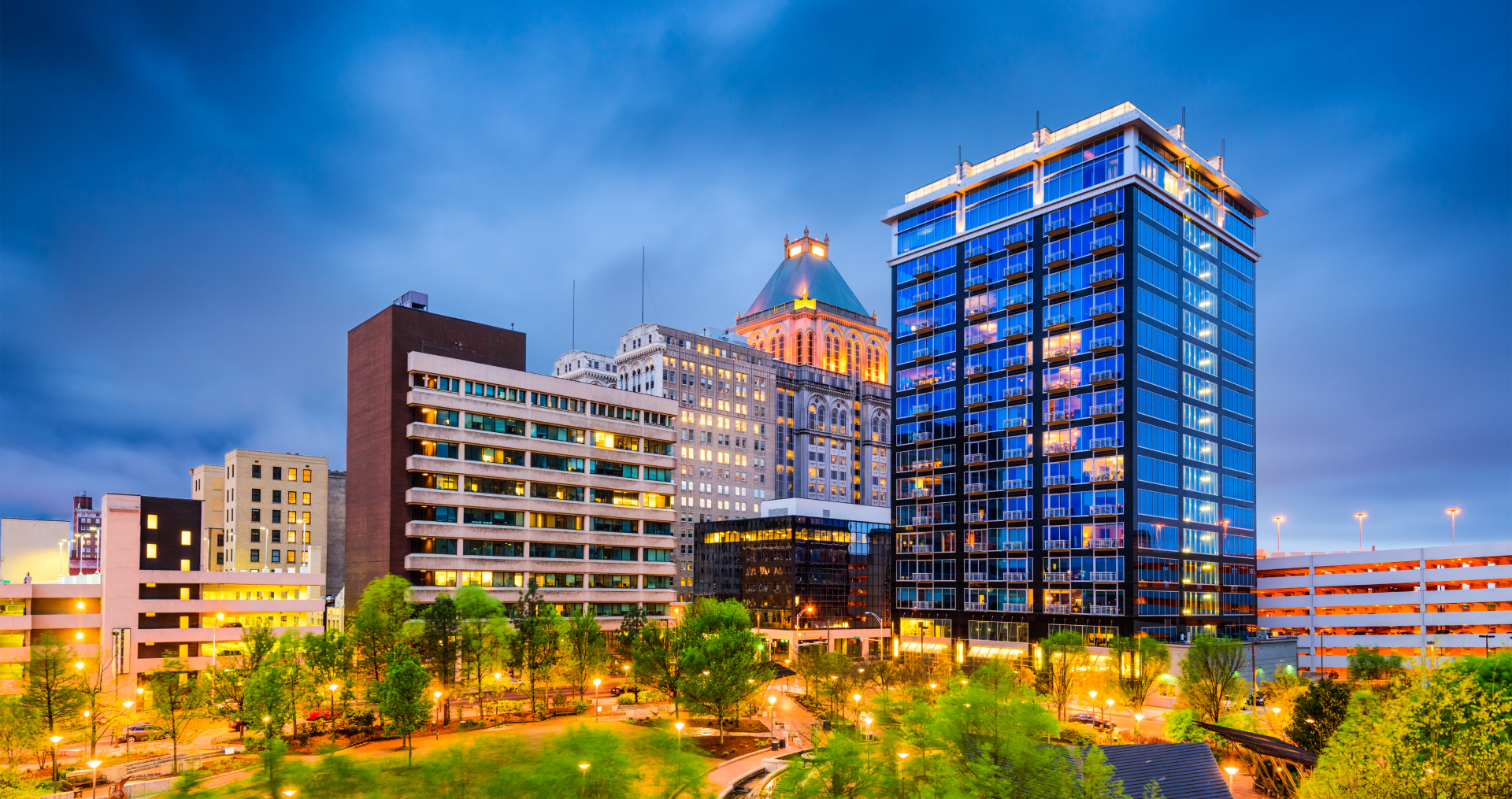 Downtown Asheville skyline at dusk, showcasing illuminated buildings against a blue sky.