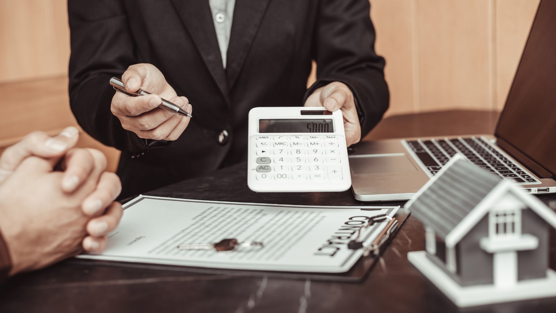 Business meeting with calculator, documents, laptop, and model house on a desk