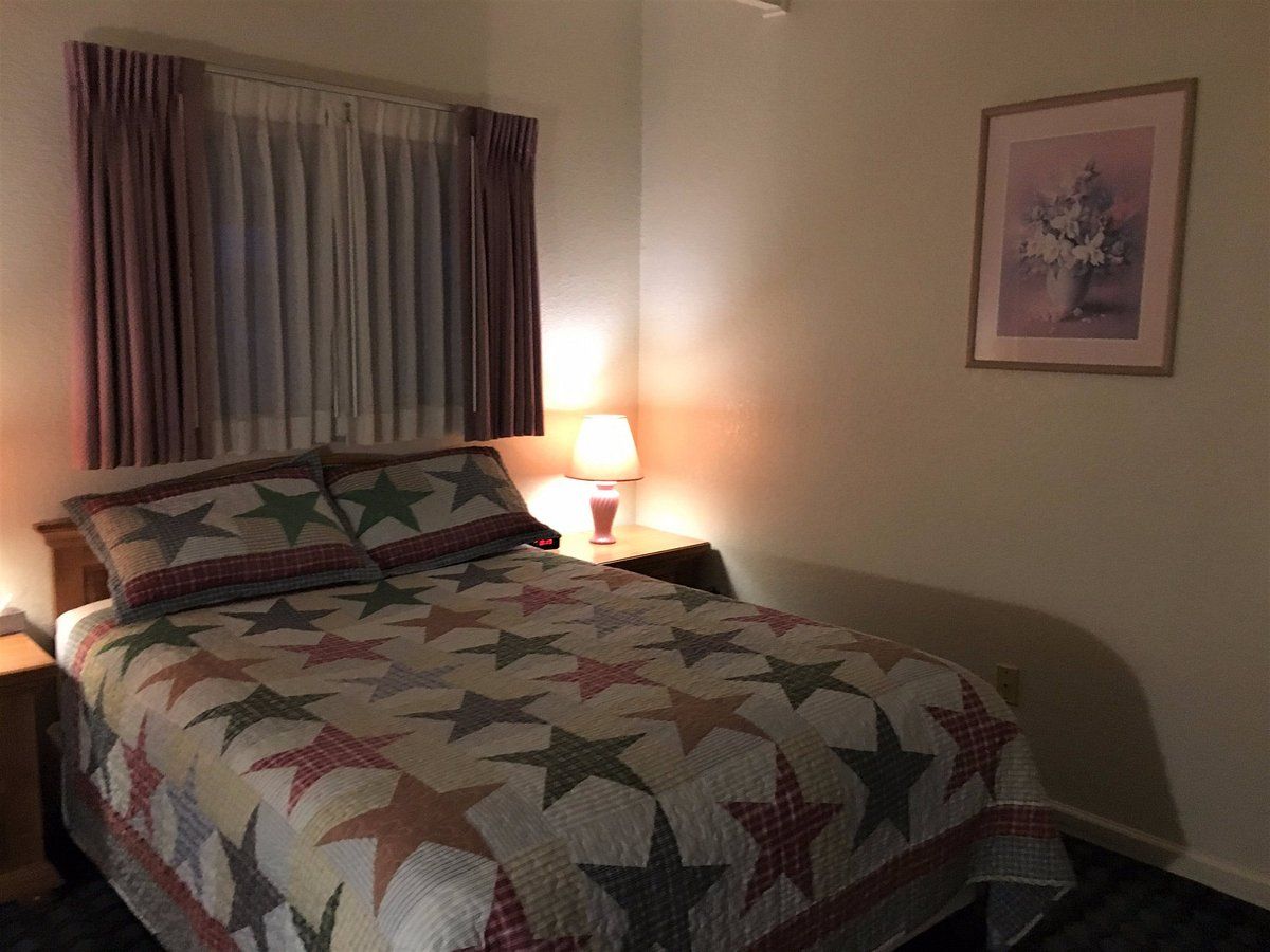A bedroom with a bed , nightstand , lamp and a picture on the wall.