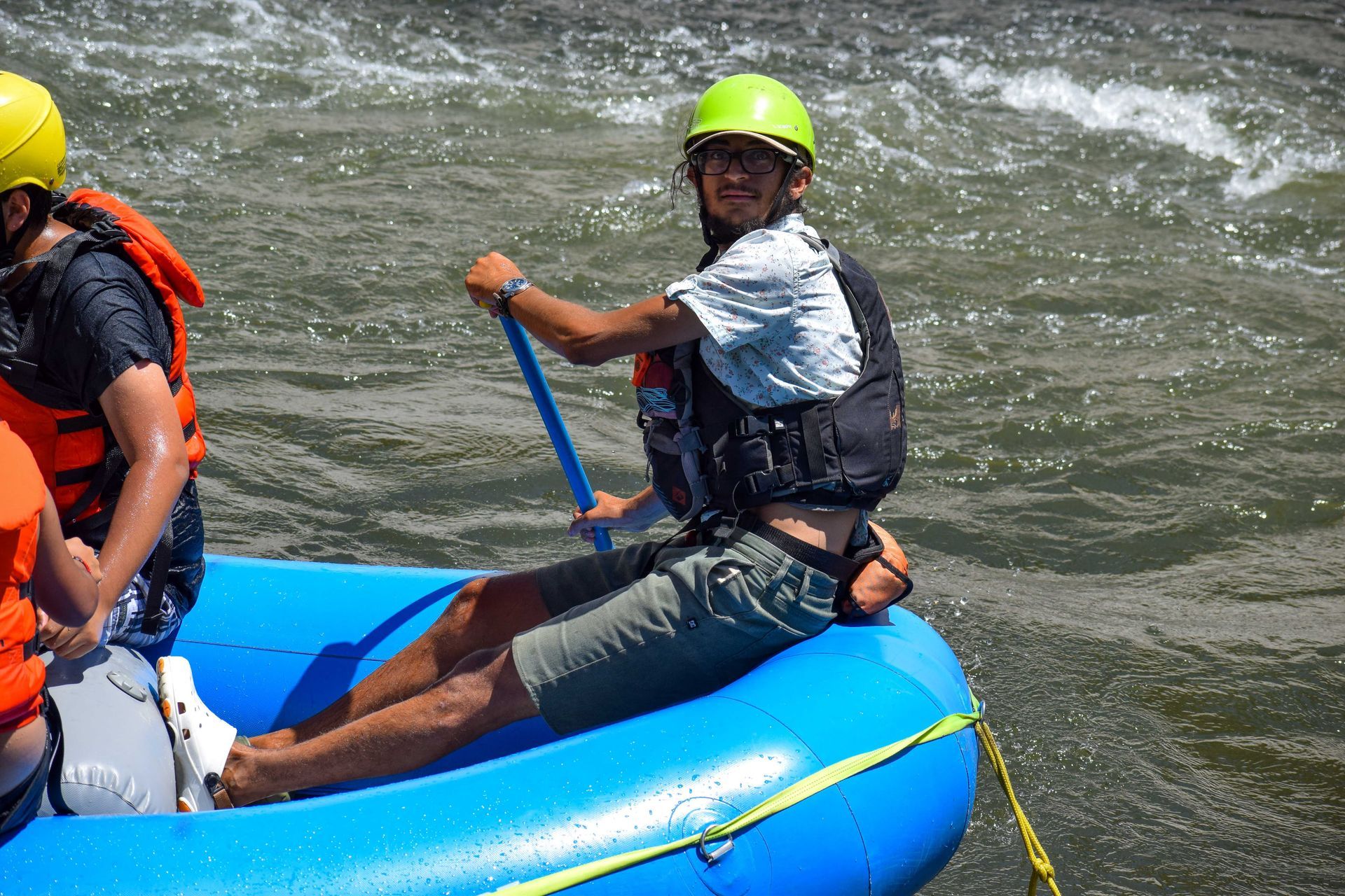 man on a blue whitewater raft with a yellow helmet 