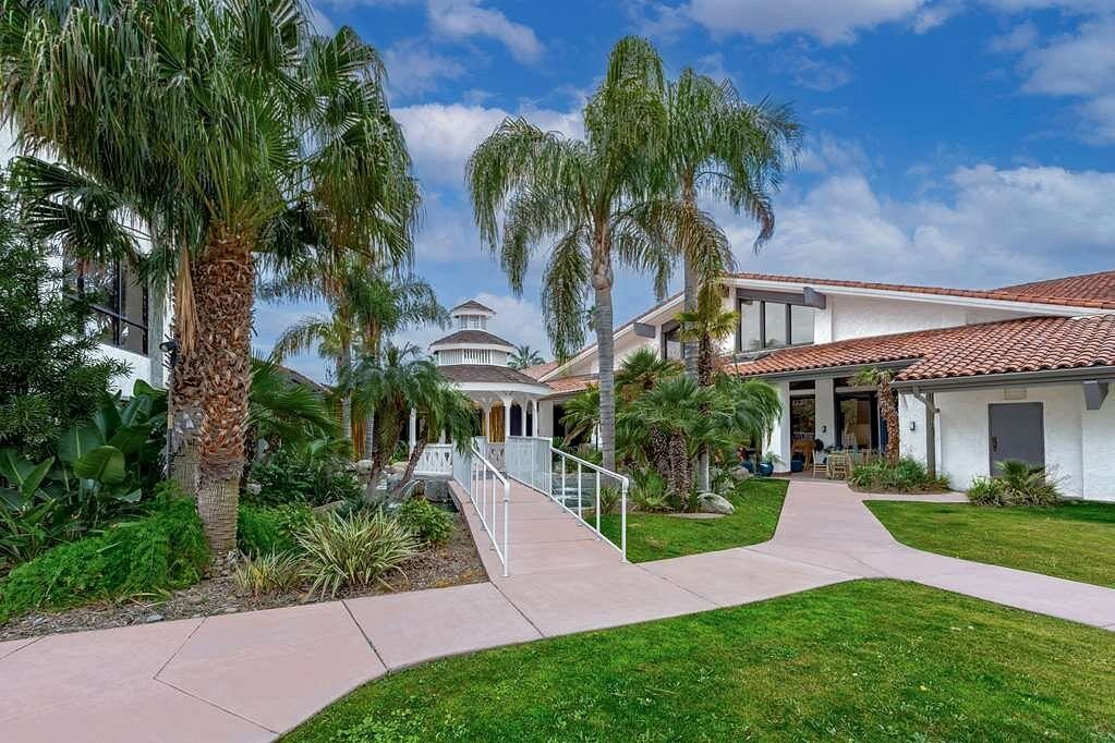 A large white house with a walkway leading to it surrounded by palm trees.