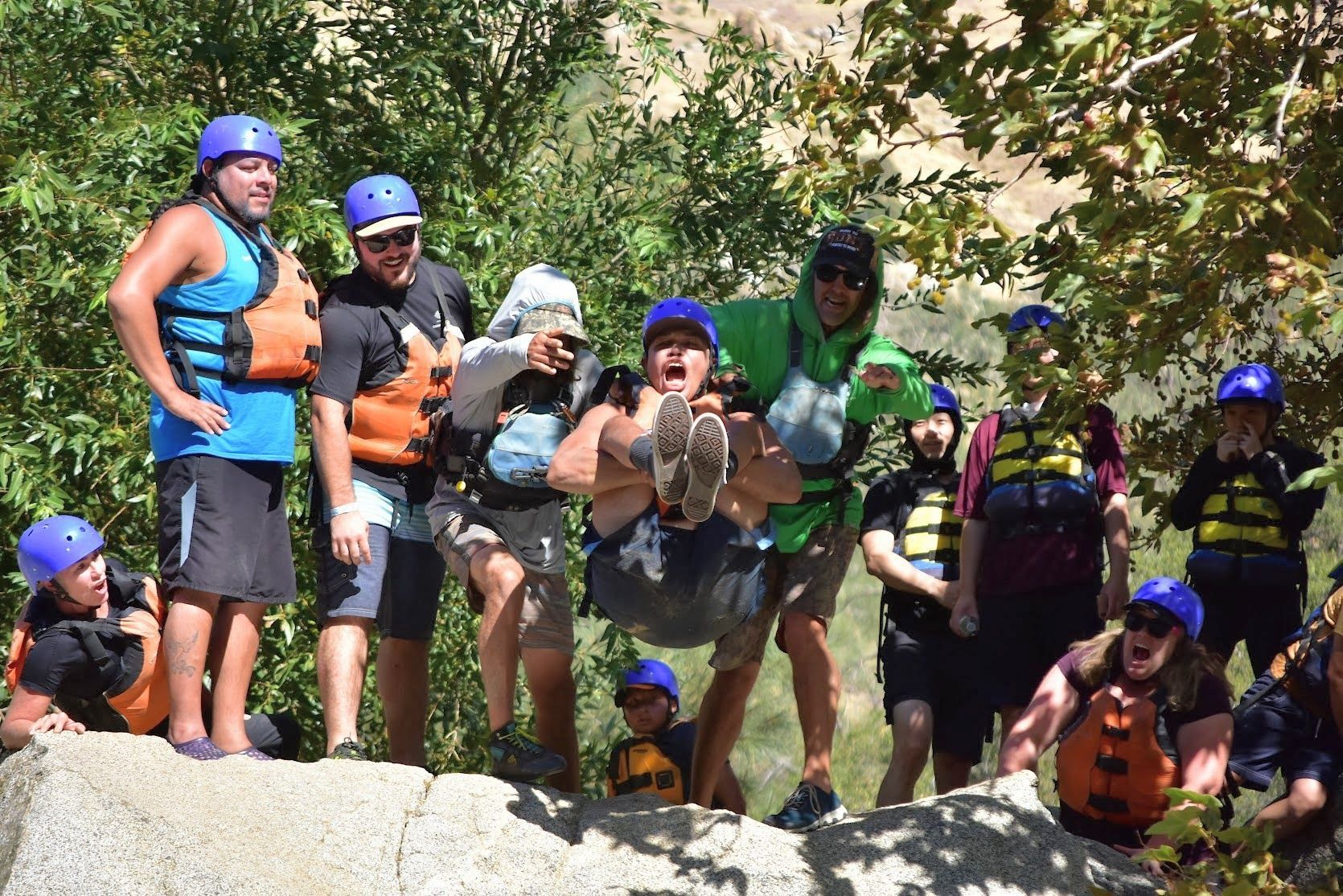 A group of people wearing life jackets are standing around a rock. 