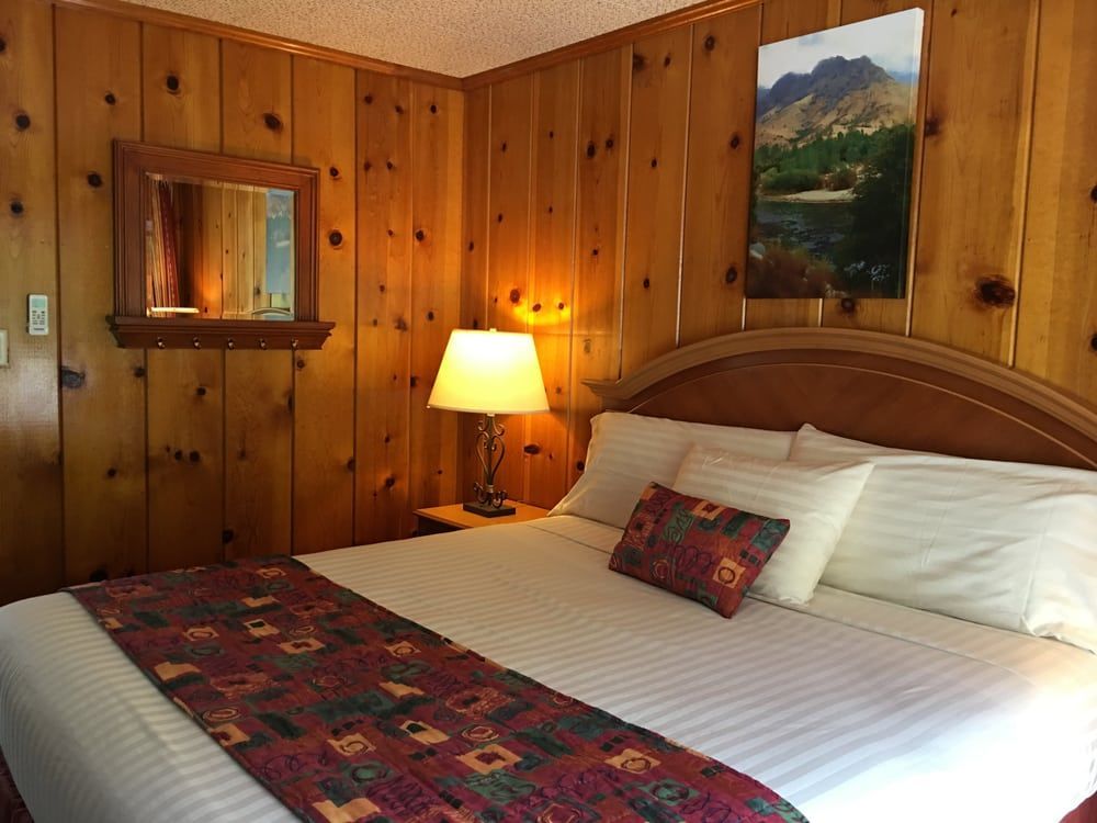 A hotel room with a bed , lamp , mirror and wood paneling