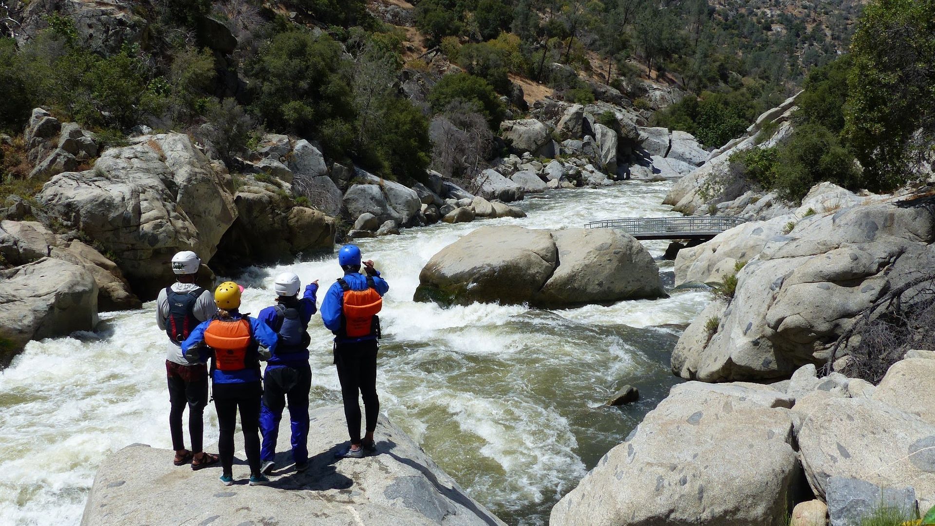 Group of hikers in life jackets standing by a rushing river among rocky cliffs
