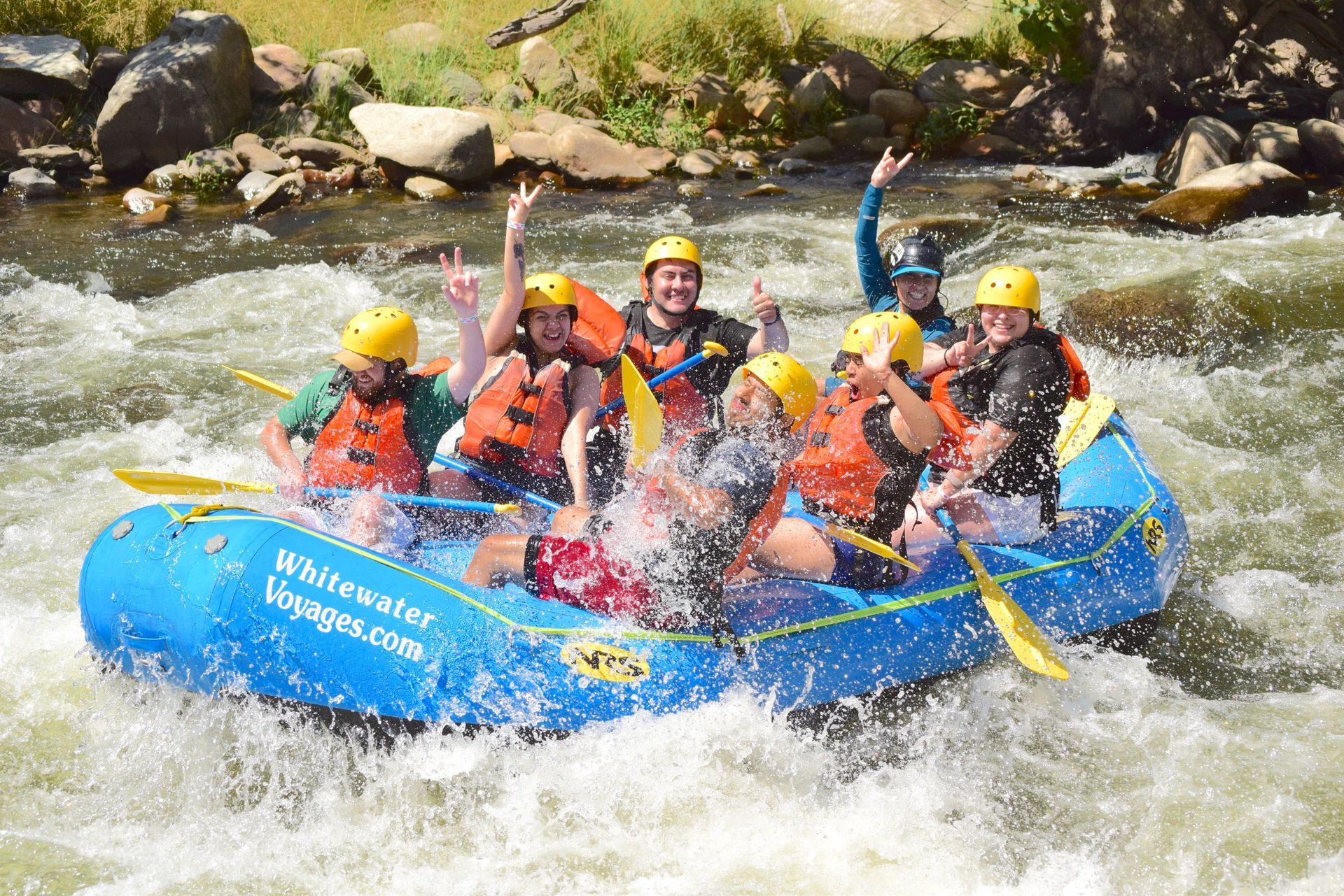 A group in a raft smiling with their hands in the air