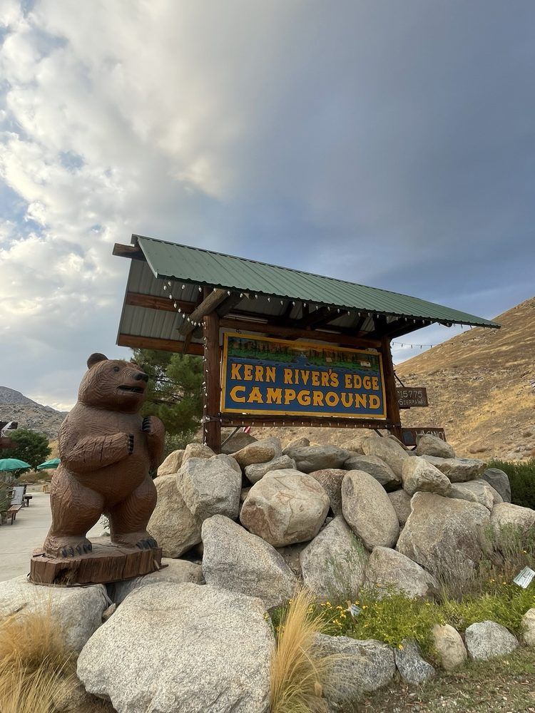 A statue of a bear is standing in front of a sign for a campground.