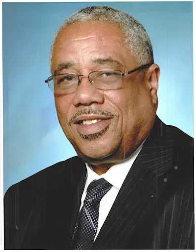 Studio portrait of a man in a dark suit and tie against a blue background