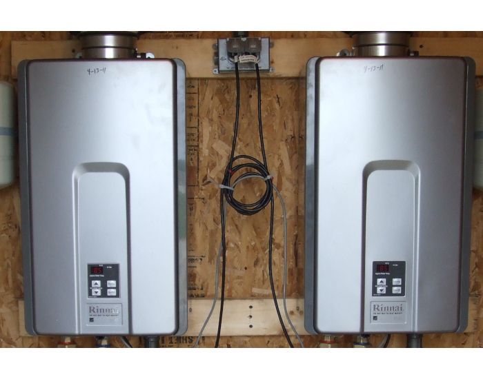 Two silver tankless water heaters mounted on wooden wall.