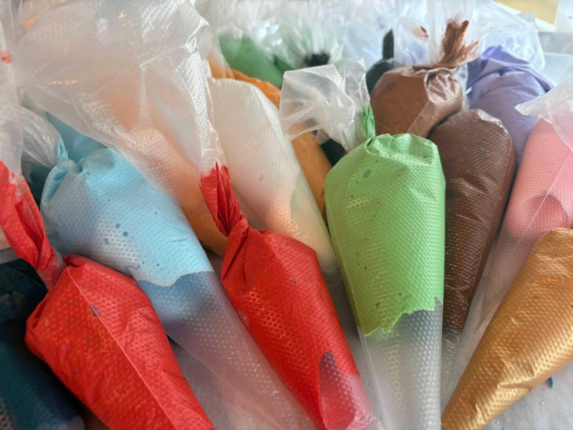 Colorful icing in disposable piping bags ready for decorating. Base Camp Bakery Gunnison, Colorado https://share.google/AgqUzUKNzsb0ThlP5, https://www.facebook.com/BaseCampBakery1, https://www.instagram.com/basecampbakery_81230