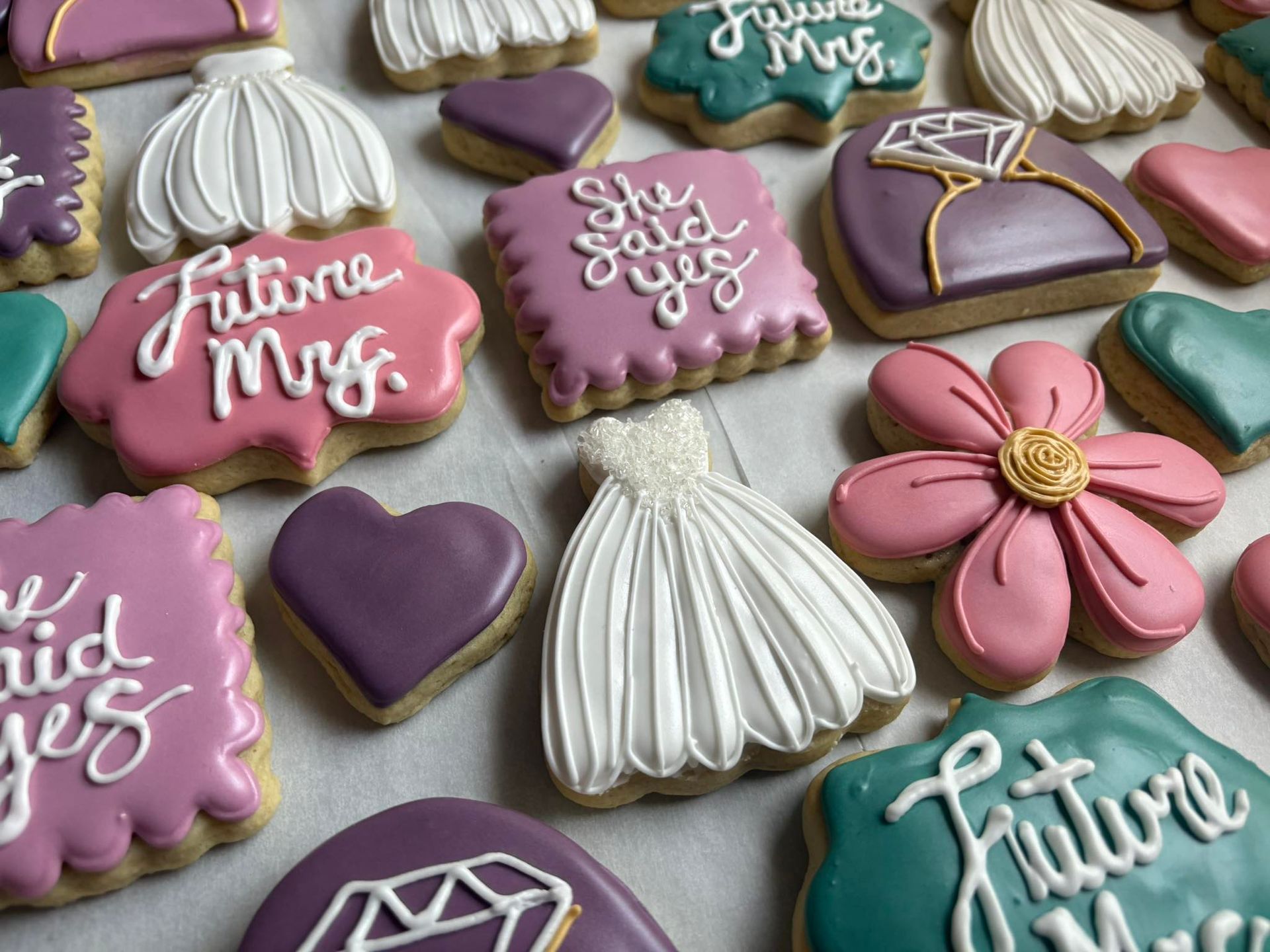 Decorated sugar cookies in various shapes and colors: wedding dresses, hearts, engagement rings, and 