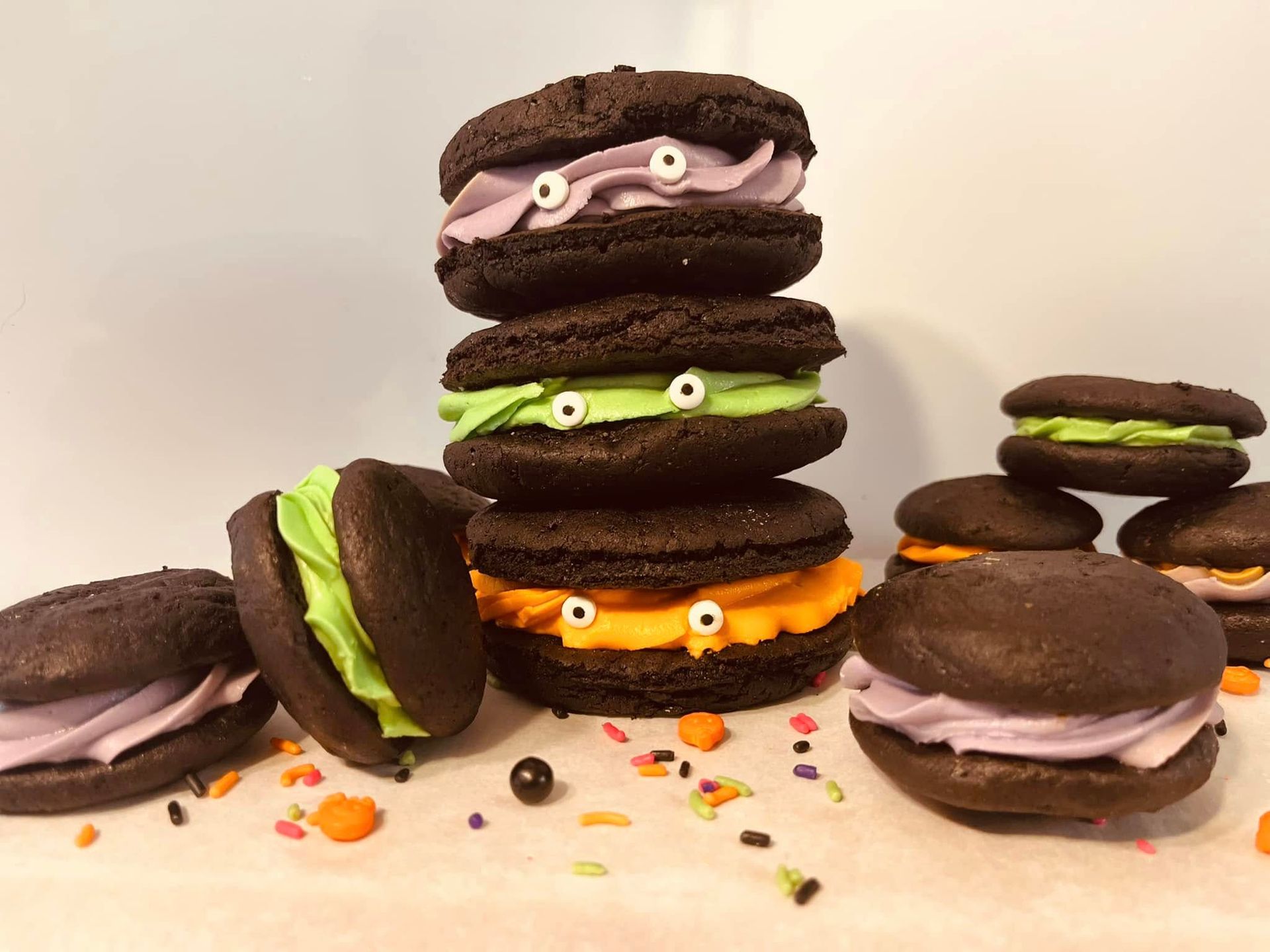 Chocolate sandwich cookies stacked and scattered with colorful frosting faces, Halloween theme. Base Camp Bakery Gunnison, Colorado https://share.google/AgqUzUKNzsb0ThlP5, https://www.facebook.com/BaseCampBakery1, https://www.instagram.com/basecampbakery_81230