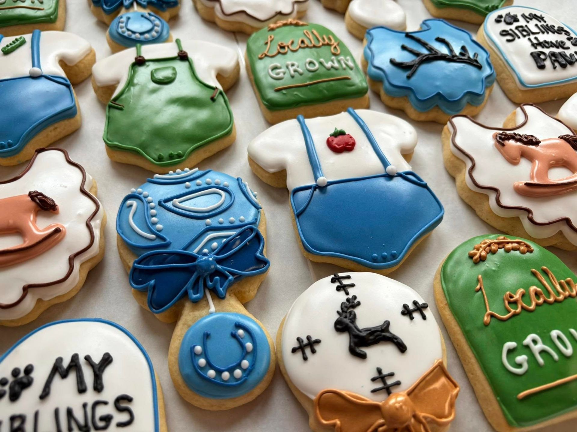 Decorated sugar cookies in shapes of baby clothes, toys, and text. Various colors, white icing. Base Camp Bakery Gunnison, Colorado https://share.google/AgqUzUKNzsb0ThlP5, https://www.facebook.com/BaseCampBakery1, https://www.instagram.com/basecampbakery_81230