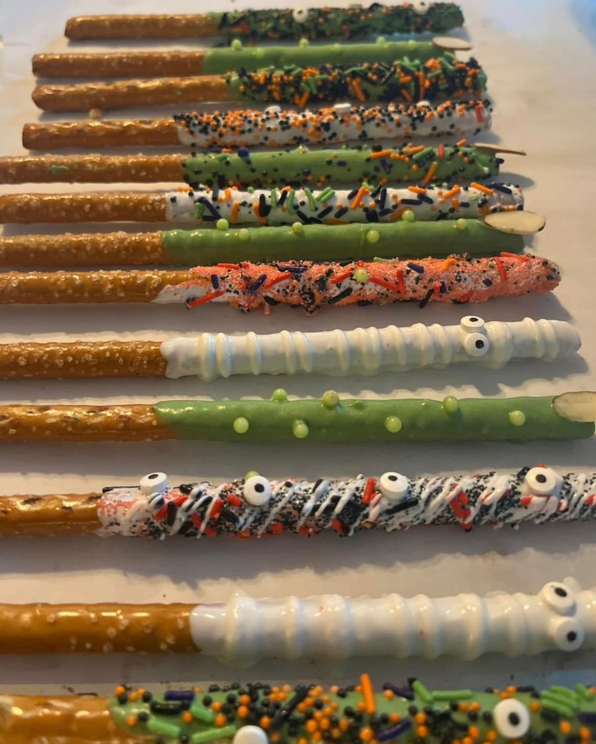 Halloween-decorated pretzel rods. Several rods dipped in white, orange, and green chocolate, with sprinkles and candy eyes. Base Camp Bakery Gunnison, Colorado https://share.google/AgqUzUKNzsb0ThlP5, https://www.facebook.com/BaseCampBakery1, https://www.instagram.com/basecampbakery_81230