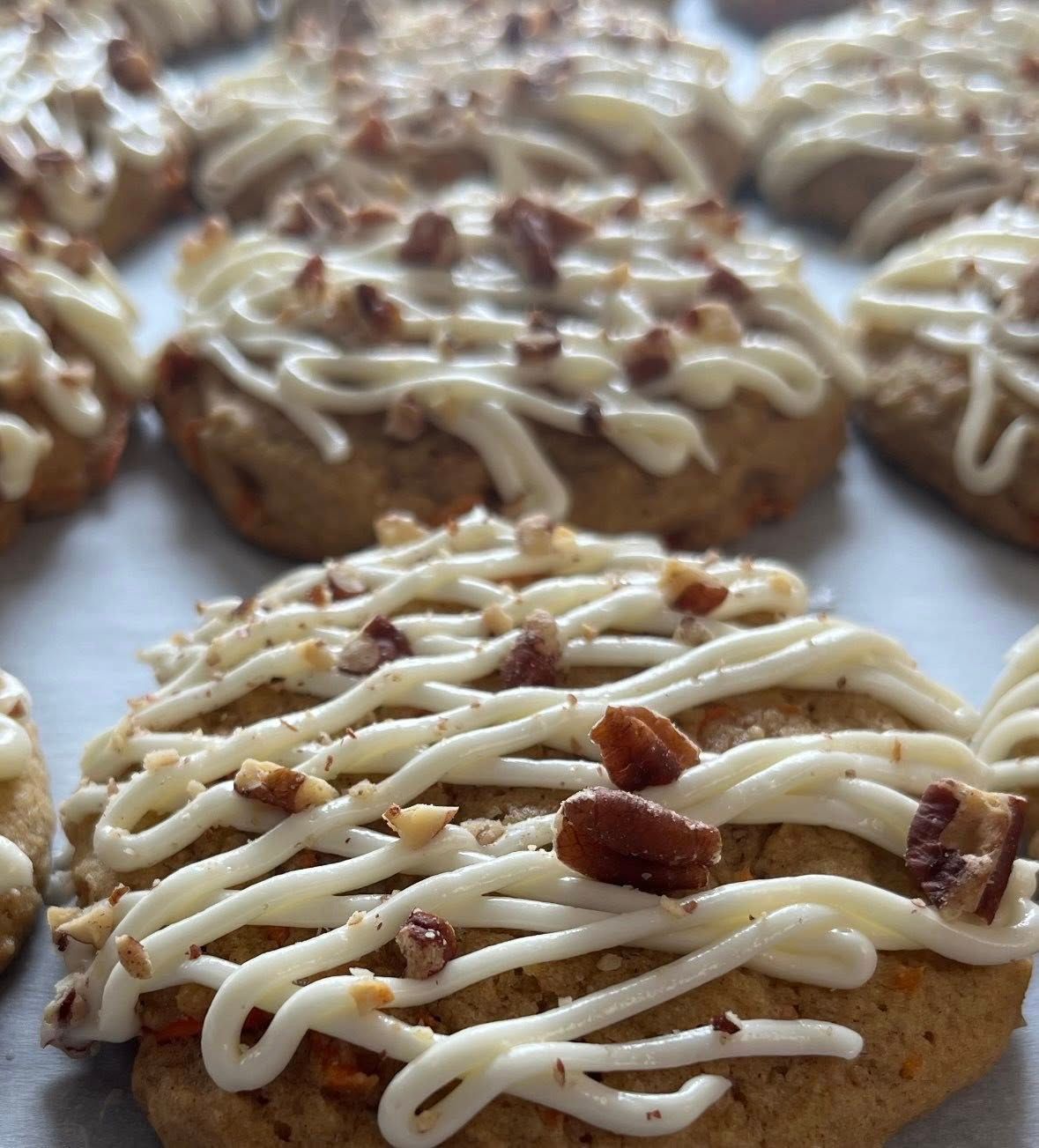 Frosted carrot cake cookies with chopped nuts, arranged on parchment paper. Base Camp Bakery Gunnison, Colorado https://share.google/AgqUzUKNzsb0ThlP5, https://www.facebook.com/BaseCampBakery1, https://www.instagram.com/basecampbakery_81230