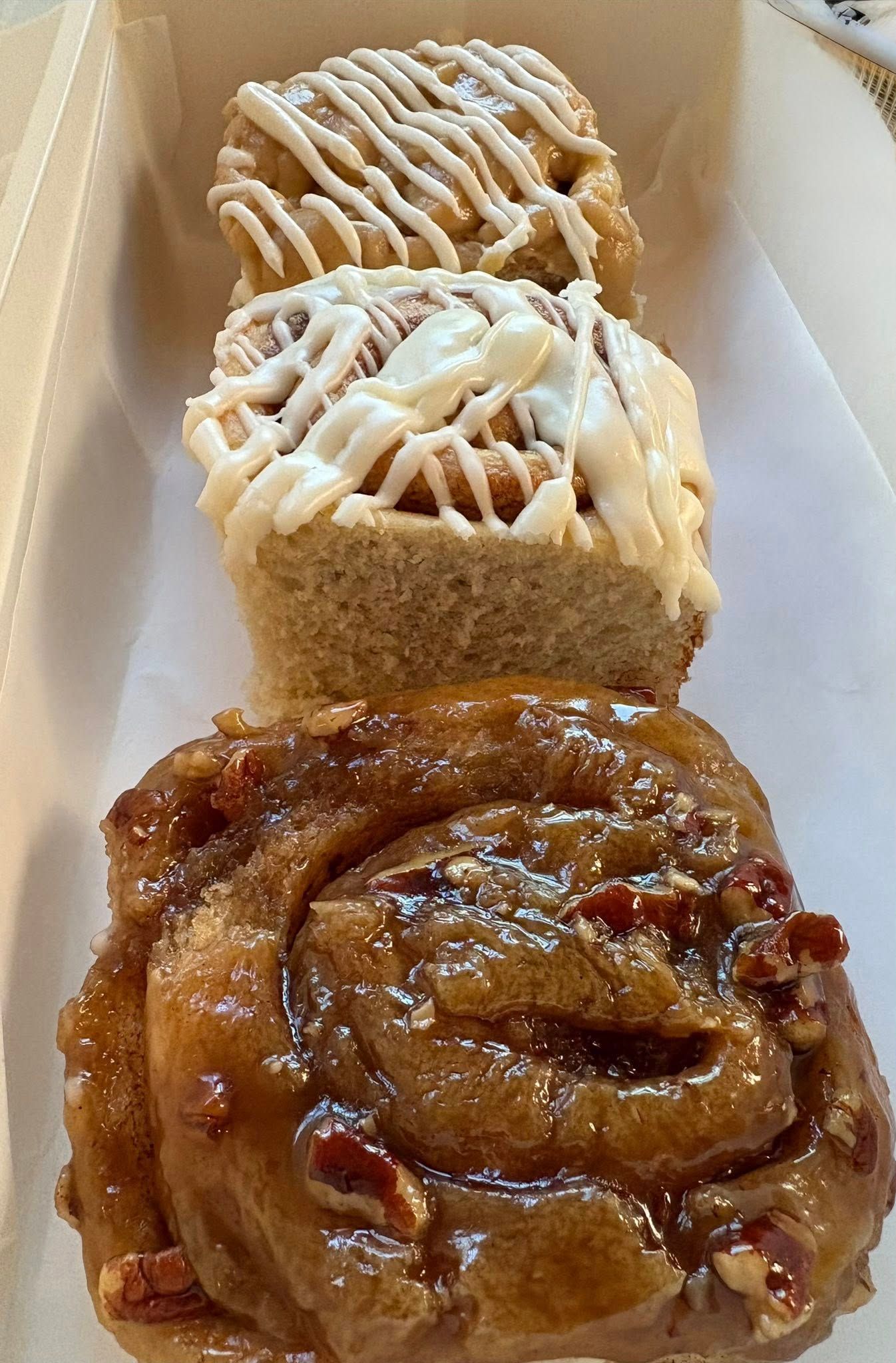 Three cinnamon rolls, one pecan, drizzled with icing, stacked in a white container. Base Camp Bakery Gunnison, Colorado https://share.google/AgqUzUKNzsb0ThlP5, https://www.facebook.com/BaseCampBakery1, https://www.instagram.com/basecampbakery_81230
