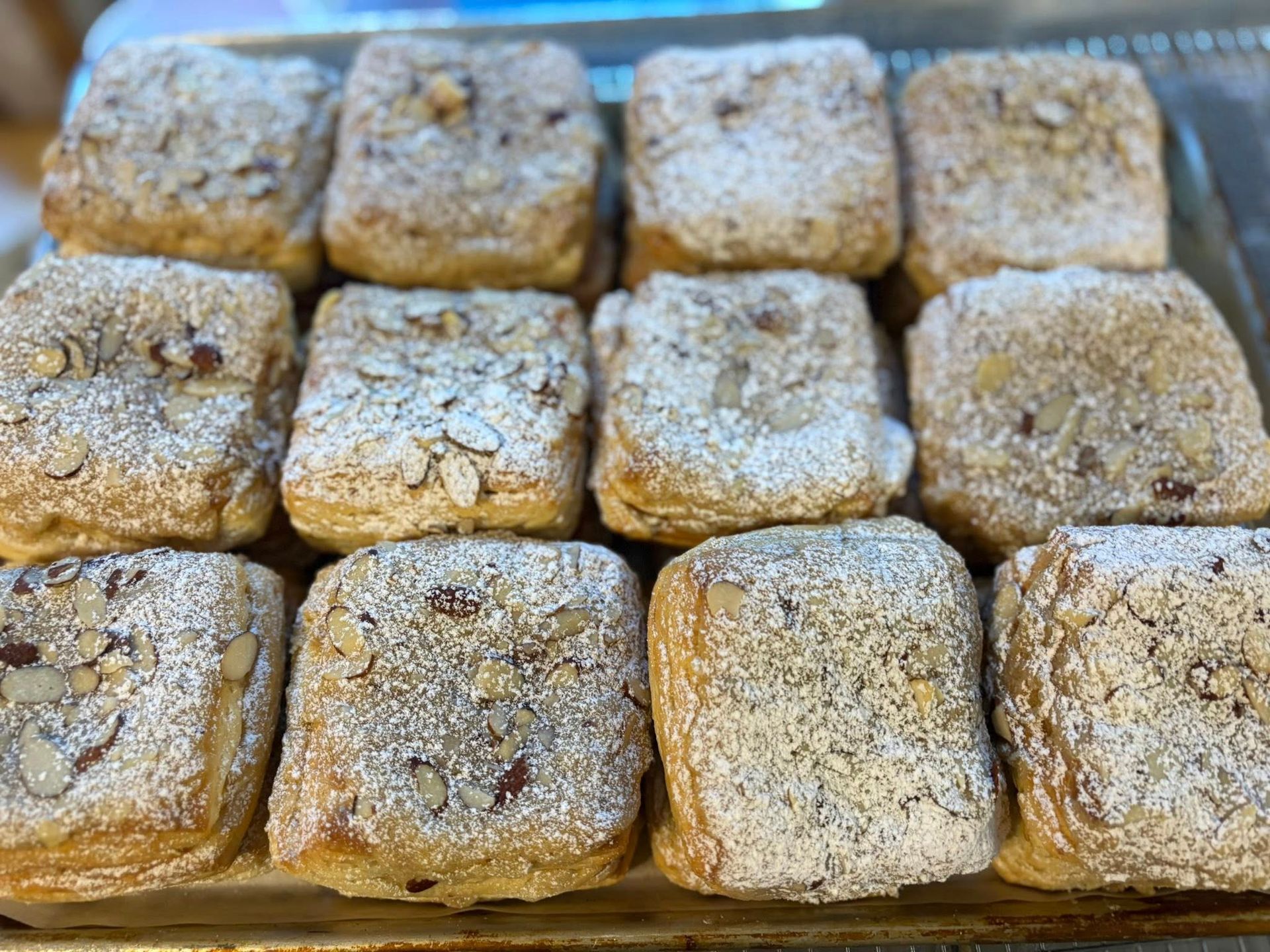 Close-up of a tray with a dozen square pastries, topped with almonds and powdered sugar. Base Camp Bakery Gunnison, Colorado https://share.google/AgqUzUKNzsb0ThlP5, https://www.facebook.com/BaseCampBakery1, https://www.instagram.com/basecampbakery_81230