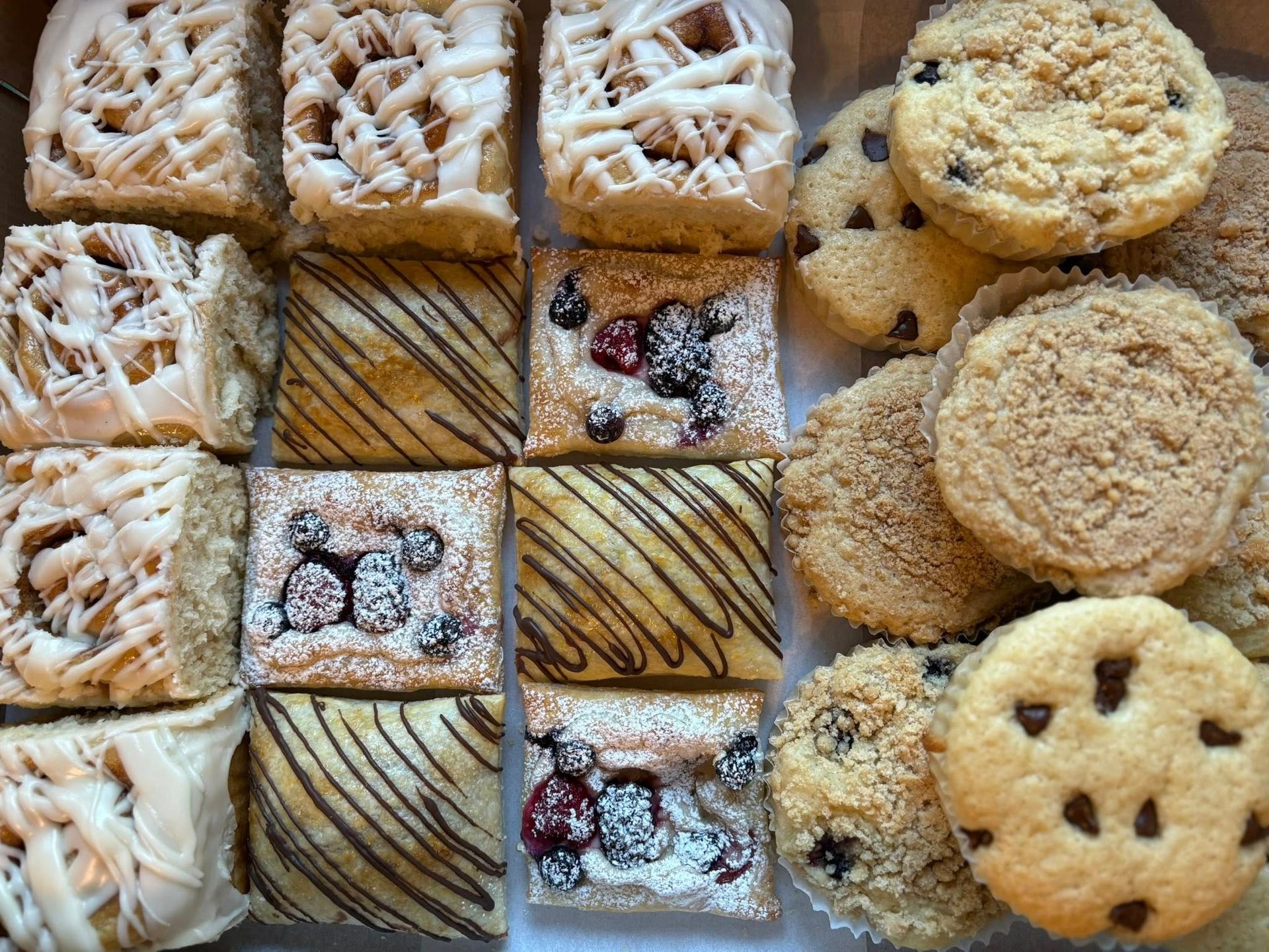 Assortment of pastries: iced squares, berry-topped squares, and chocolate chip cookies in a box. Base Camp Bakery Gunnison, Colorado https://share.google/AgqUzUKNzsb0ThlP5, https://www.facebook.com/BaseCampBakery1, https://www.instagram.com/basecampbakery_81230