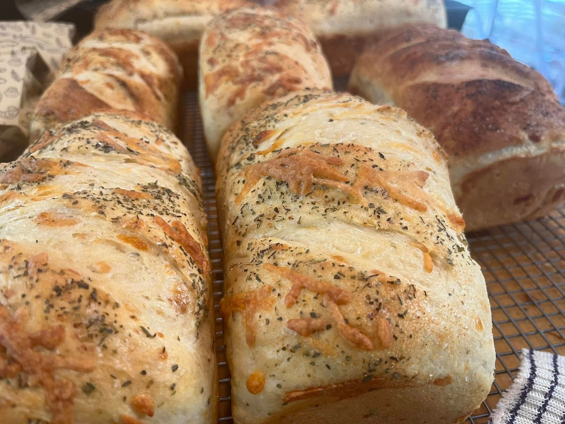 Loaves of bread topped with herbs and cheese on a wire rack. Base Camp Bakery Gunnison, Colorado https://share.google/AgqUzUKNzsb0ThlP5, https://www.facebook.com/BaseCampBakery1, https://www.instagram.com/basecampbakery_81230